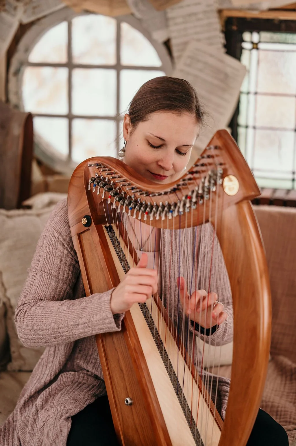 Une harpiste joue d'une harpe de thérapie dans un intérieur avec une fenêtre ronde.