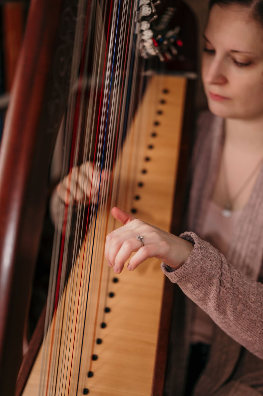 Une harpiste joue de la harpe celtique de manière calme et solenelle, de profil.