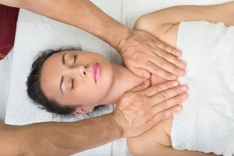 Une femme reçoit un massage thérapeutique sur le dos. Elle est allongée sur une table de massage, les yeux fermés, couverte d'une serviette blanche.