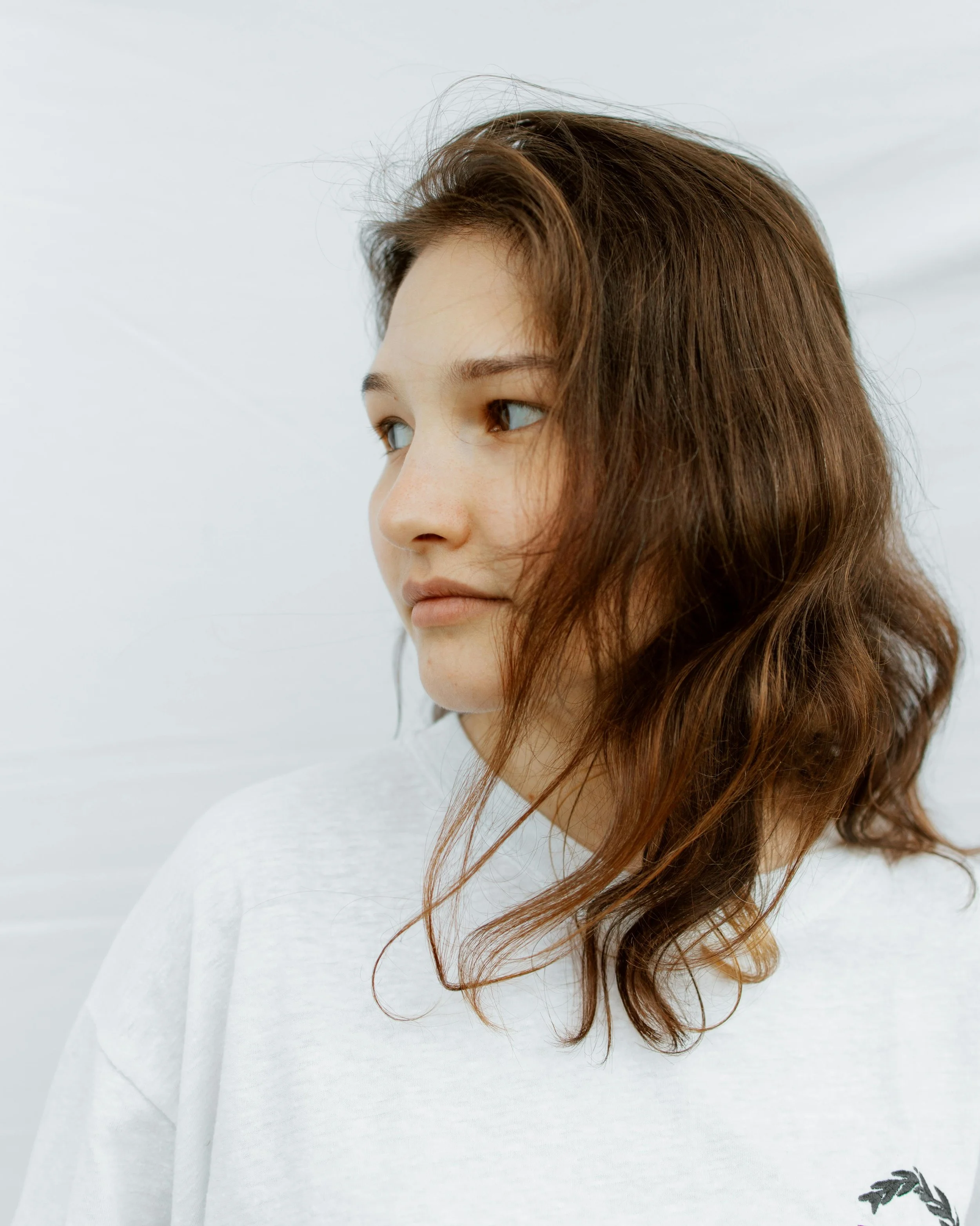 Close-up of a woman's face with brown hair, wearing a white top with a small black floral design at the bottom right.