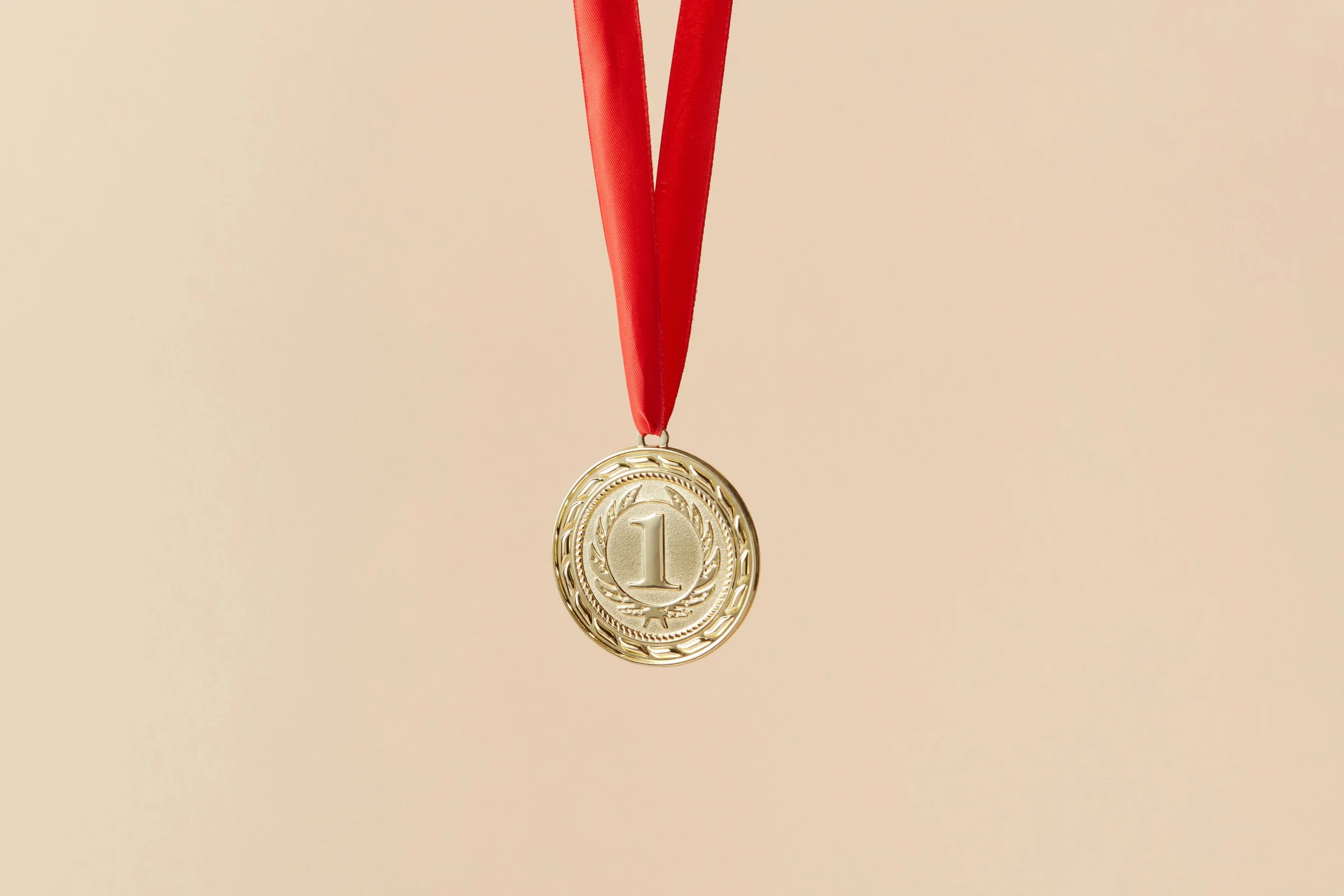 Gold medal with a red ribbon hanging against a light beige background.