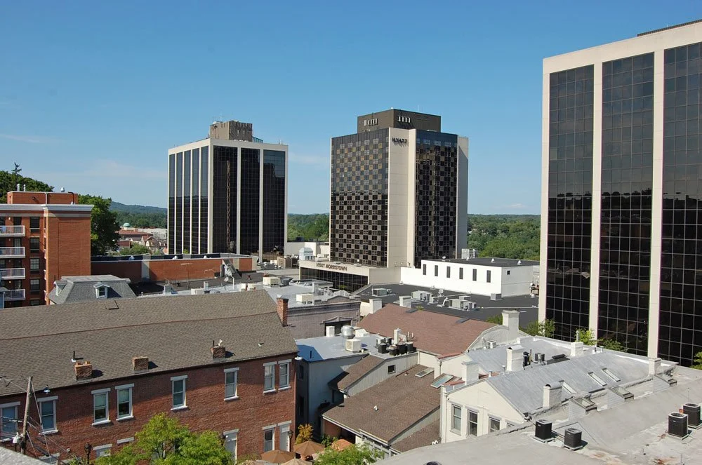 Cityscape with modern high-rise buildings and older residential rooftops under a clear blue sky.