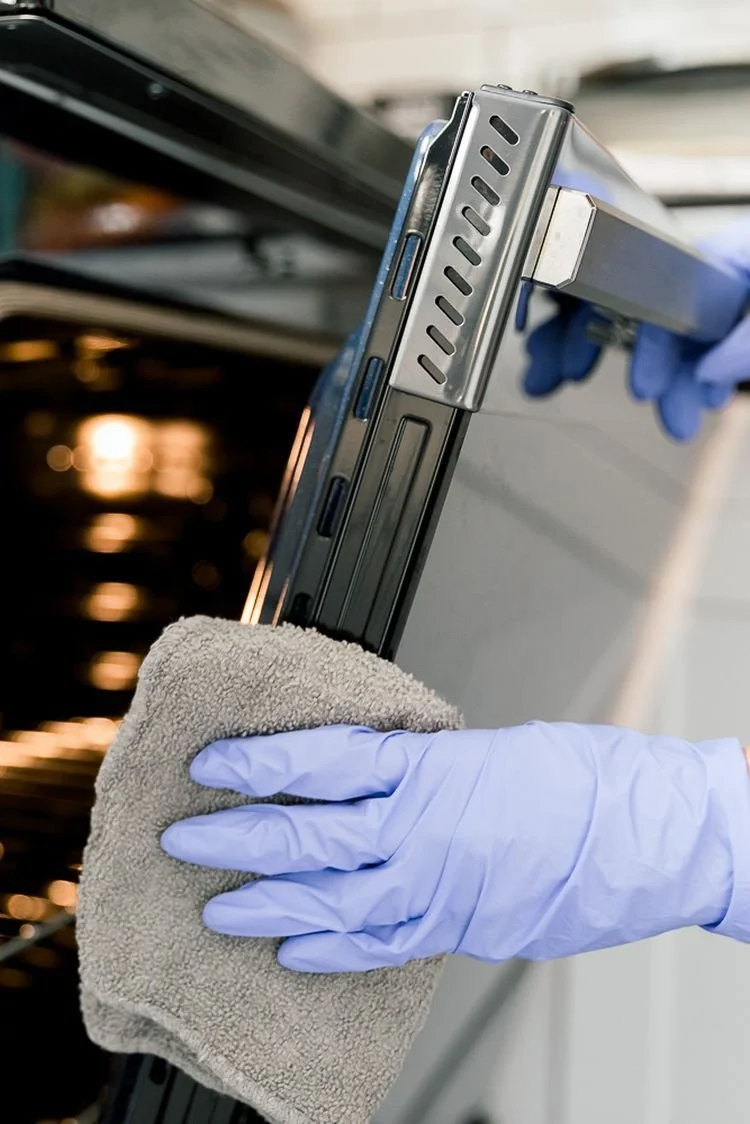 Person wearing blue gloves cleaning a laptop with a gray cloth.
