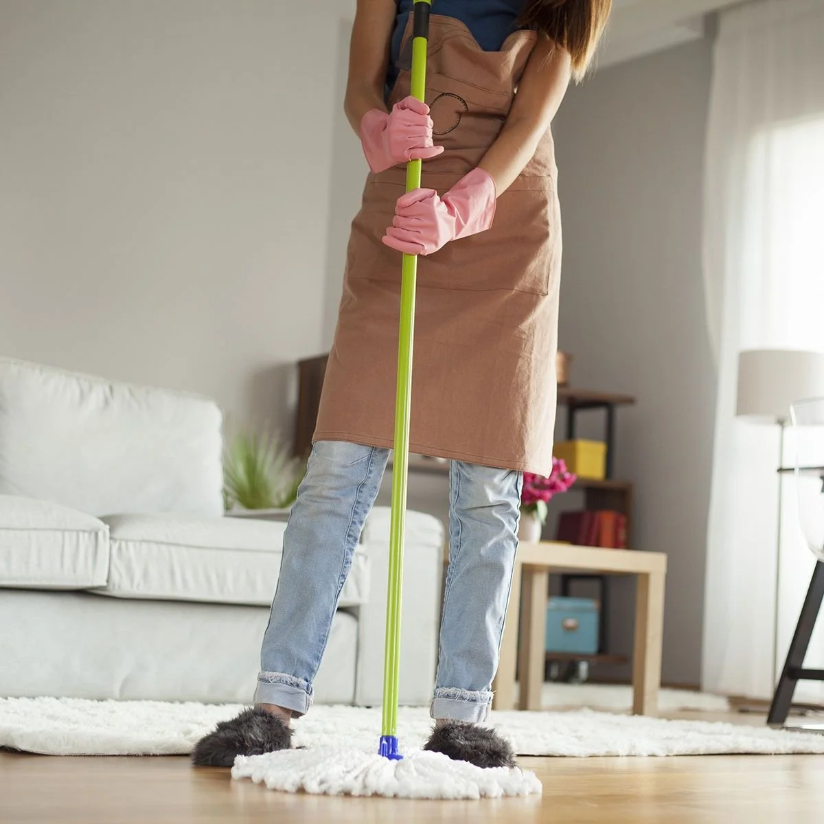 Person cleaning the floor with a mop while wearing pink rubber gloves in a living room.