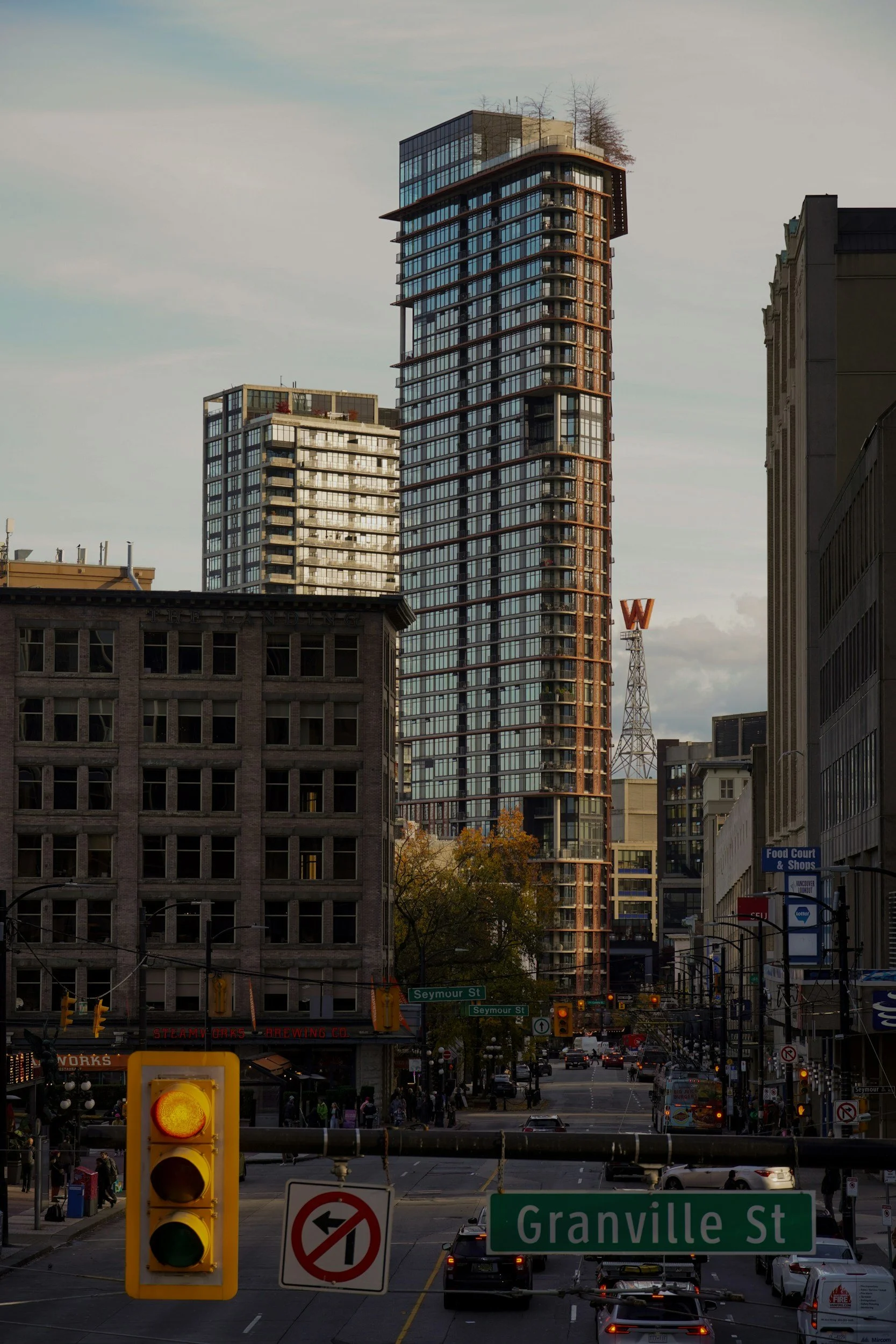 Urban street scene with tall modern glass skyscraper in the background, smaller older building in the foreground, and traffic lights and street signs for Granville Street and Seymour Street.