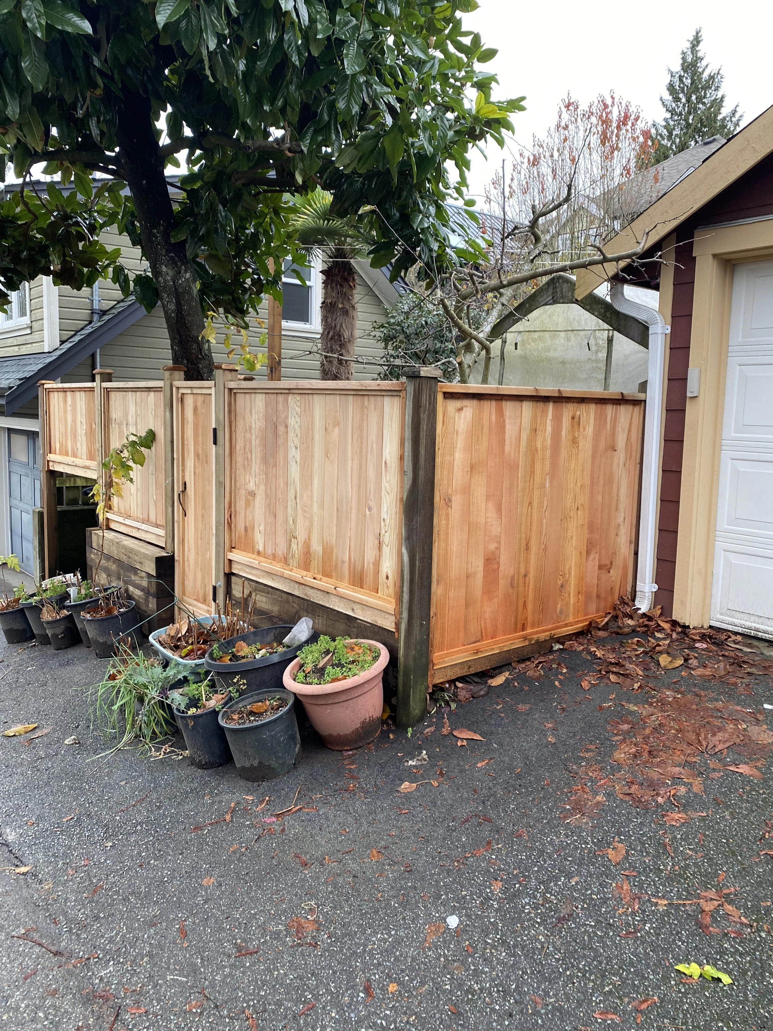 A newly built wooden privacy fence in a backyard with a paved ground, several potted plants