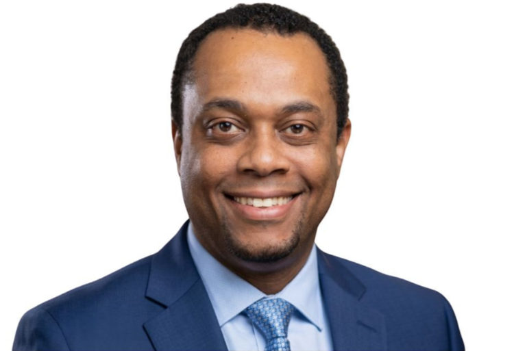 Portrait of a smiling man in a blue suit and tie against a white background.