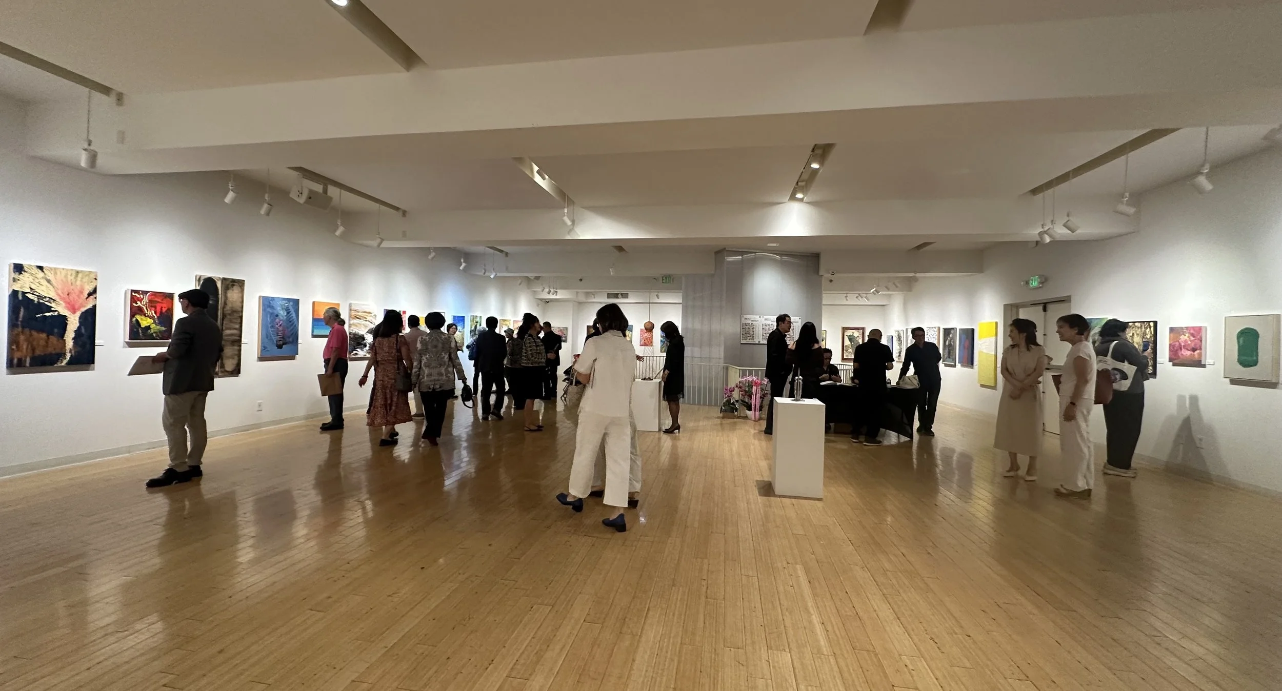 People viewing artwork in an art gallery with white walls and wooden floors.
