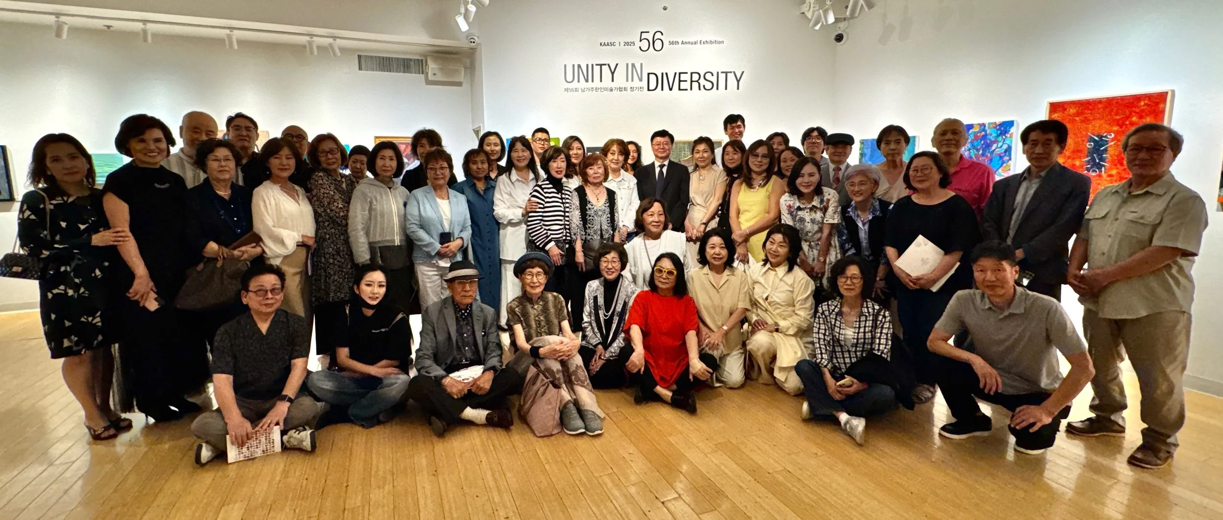 Group photo of diverse people at an art exhibition titled 'Unity in Diversity' with artworks displayed on the walls.