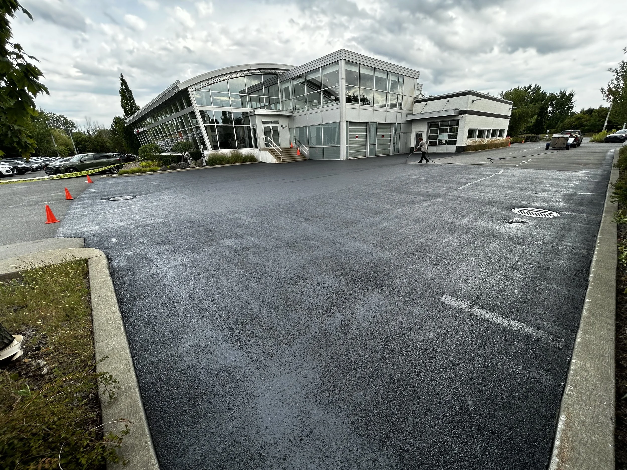 Parking neuf devant un bâtiment moderne en verre avec ciel nuageux.