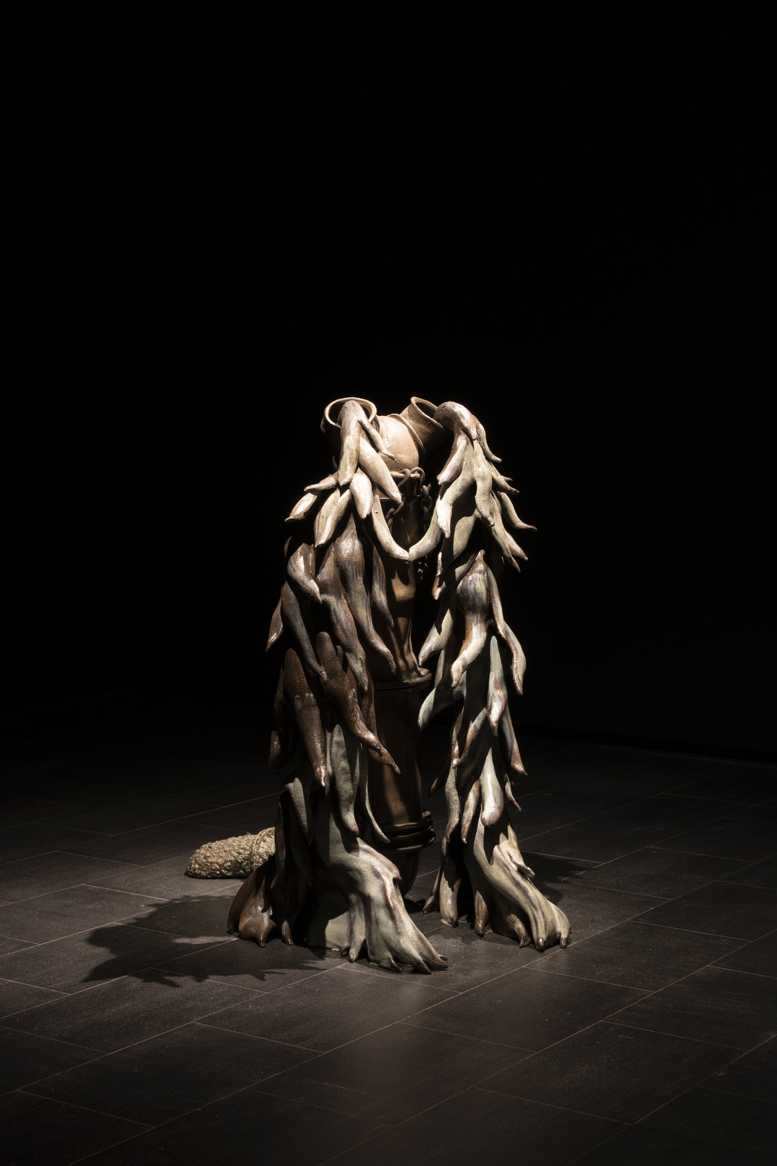 A sculpture of a face with a headdress of animal horns, made from wood and other organic materials, displayed in a dark setting.