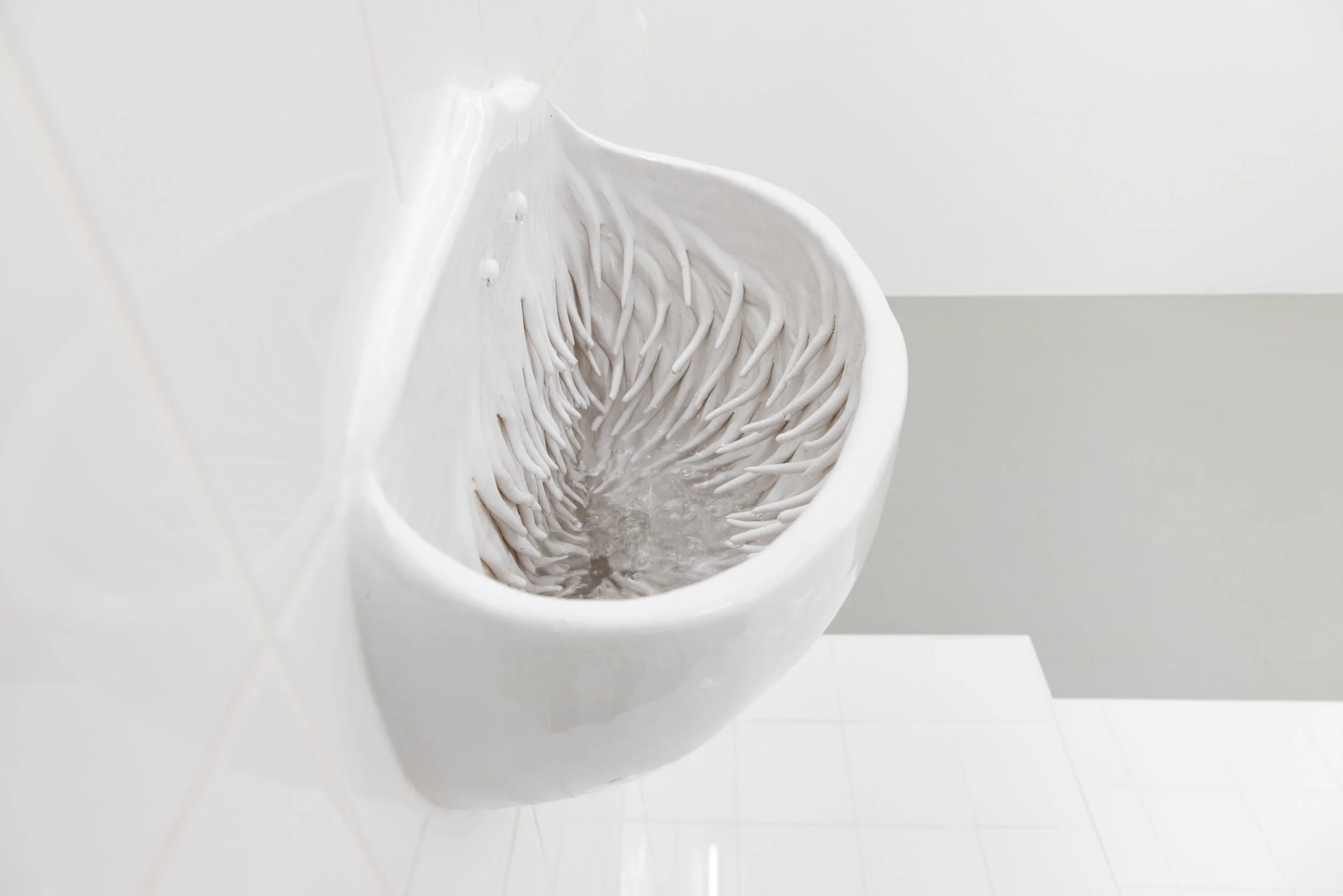 White ceramic urinal with water flowing in a bathroom.