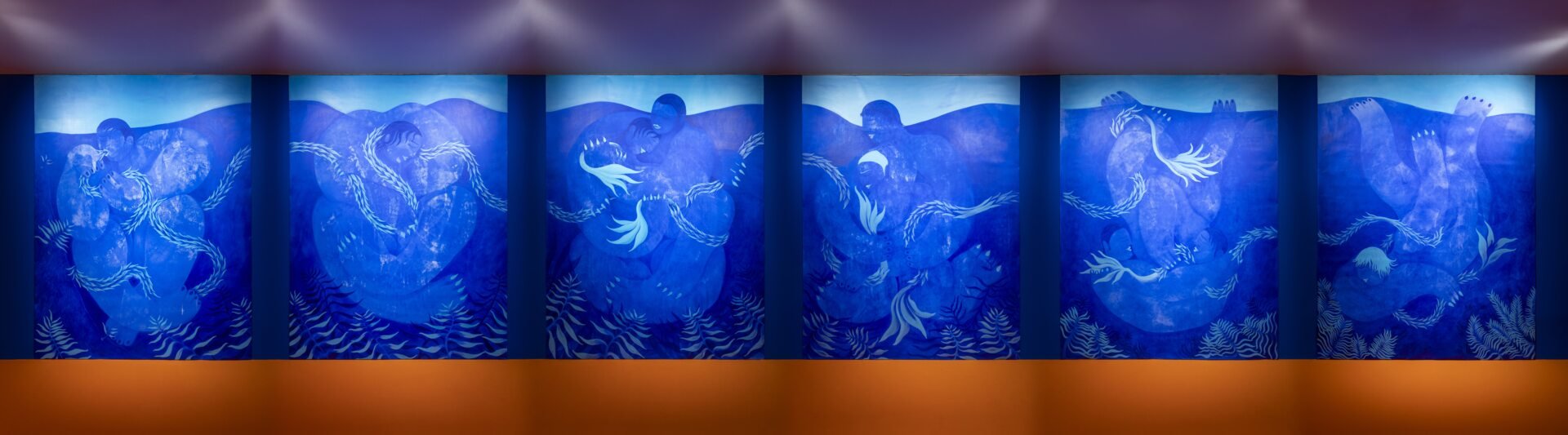 A series of six large blue panels depicting mythological sea creatures in a traditional Japanese art style, displayed on a wall with a wooden floor in front.