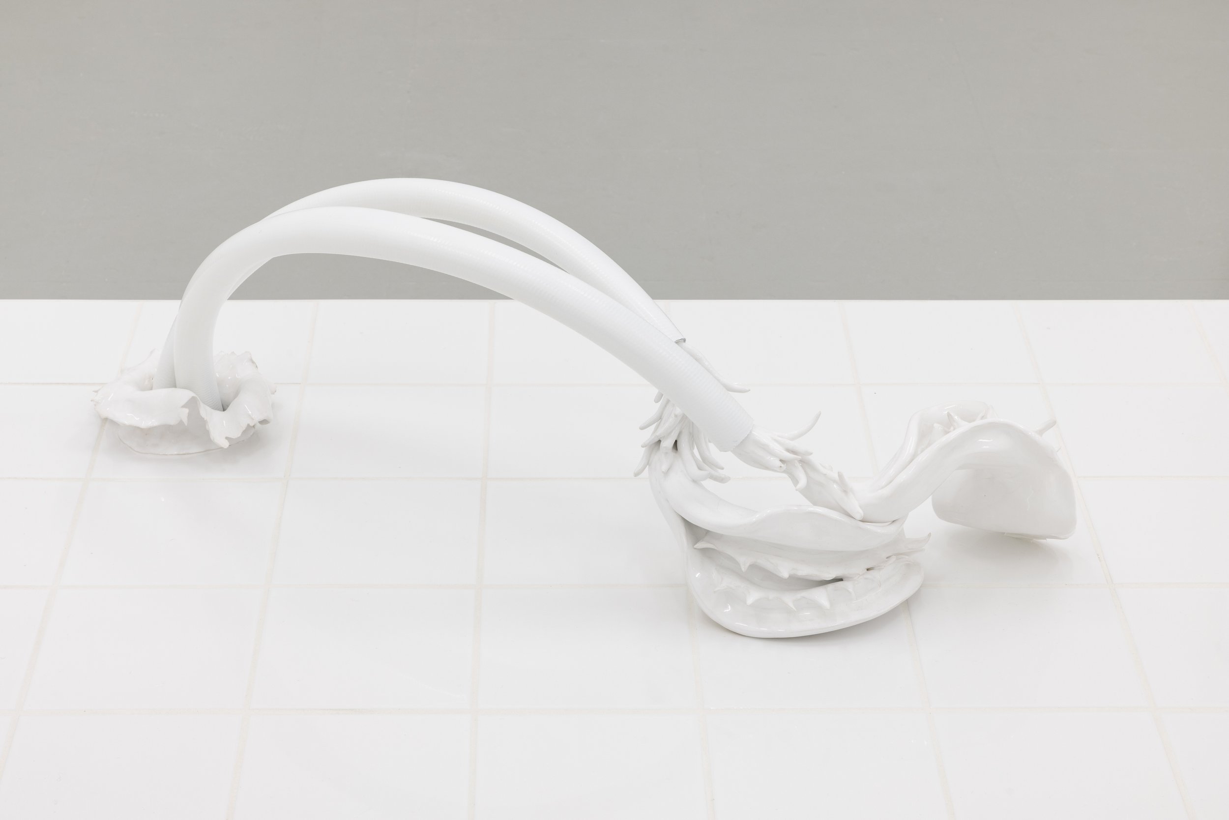 Contemporary white sculpture resembling a whale, placed on a white tiled surface with a gray background.