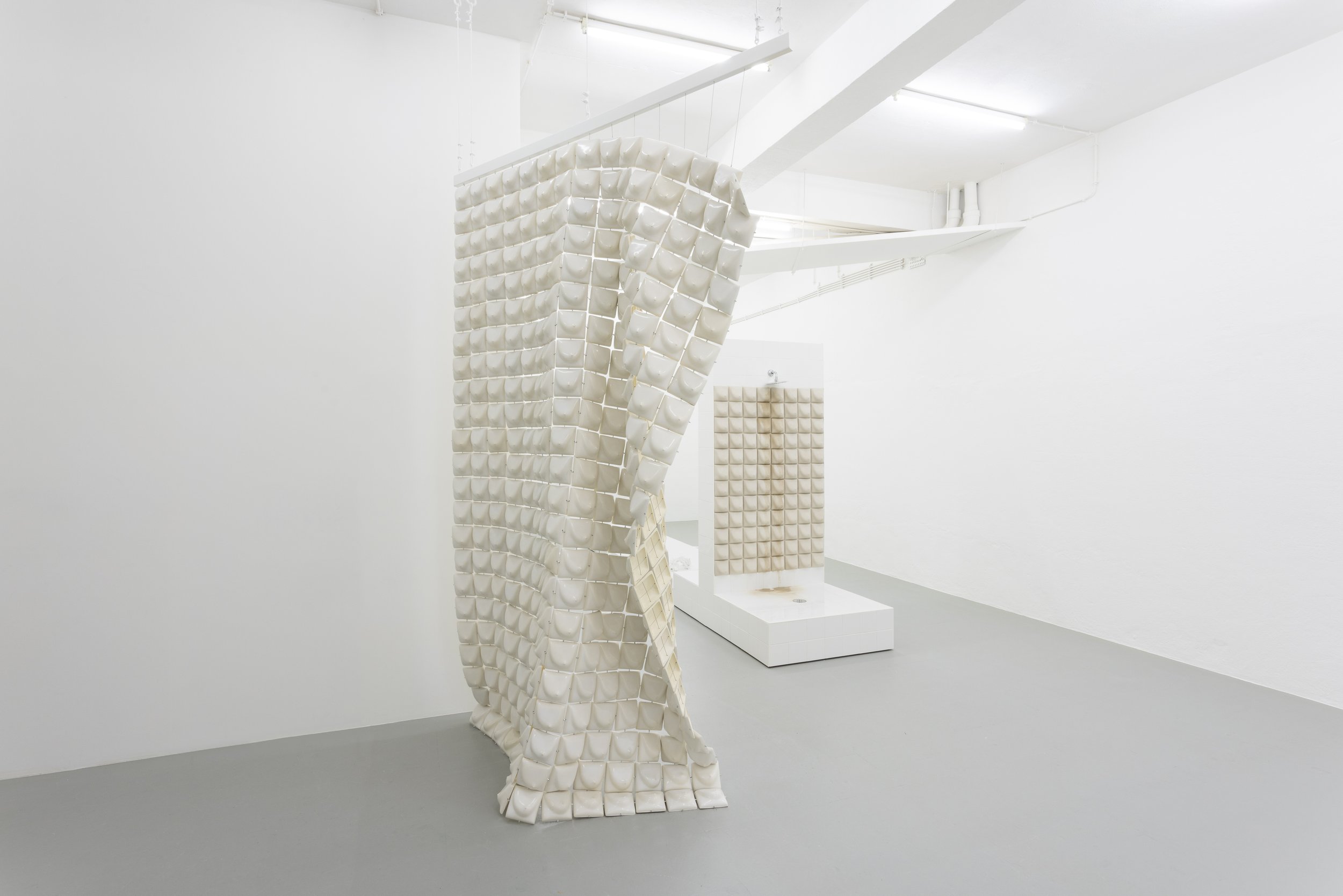Minimalist white art installation with textured, grid-like sculptures in a gallery space with white walls and gray floor.