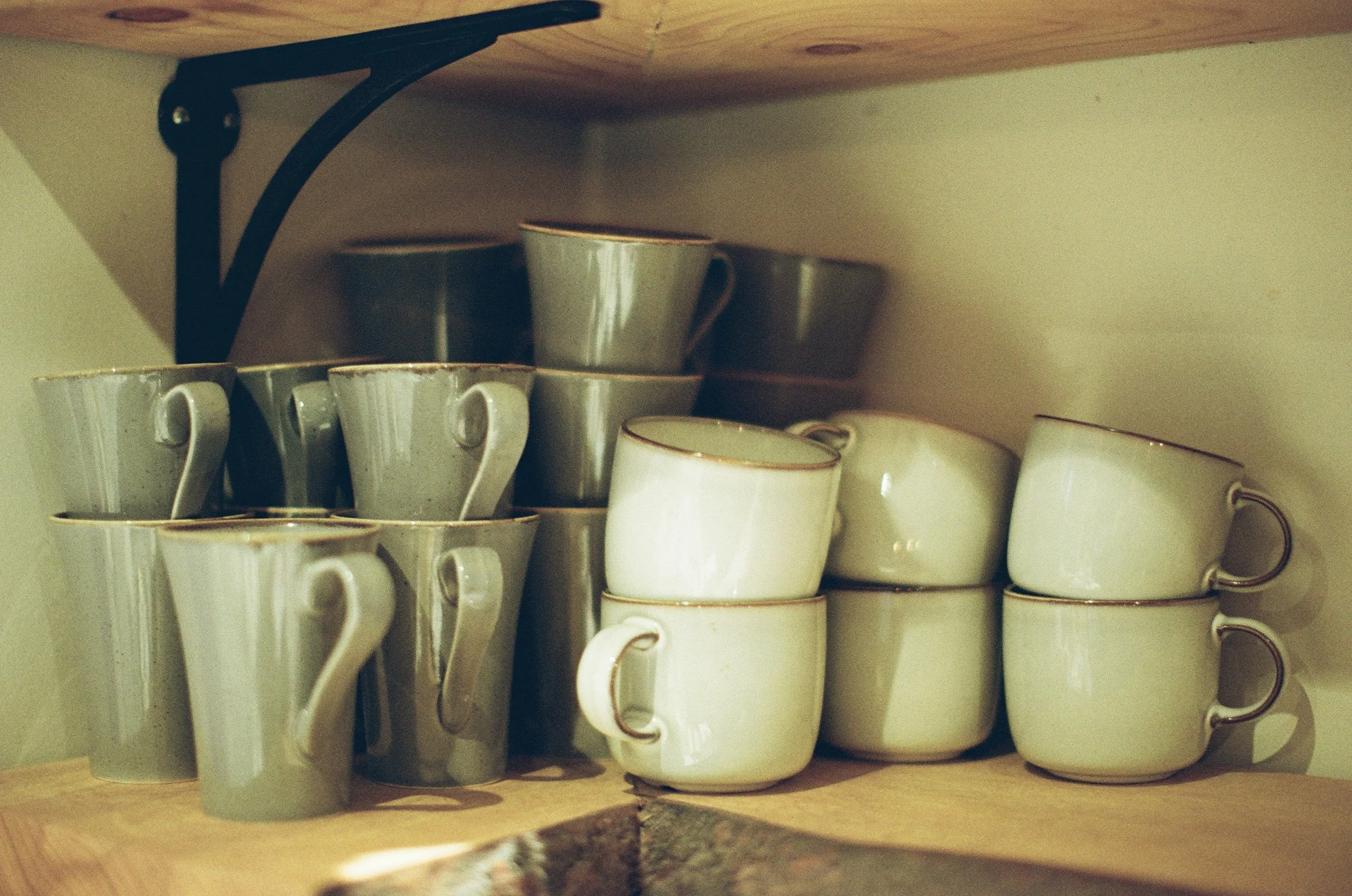 A collection of white ceramic coffee mugs with gold rims on a wooden shelf inside a cupboard.