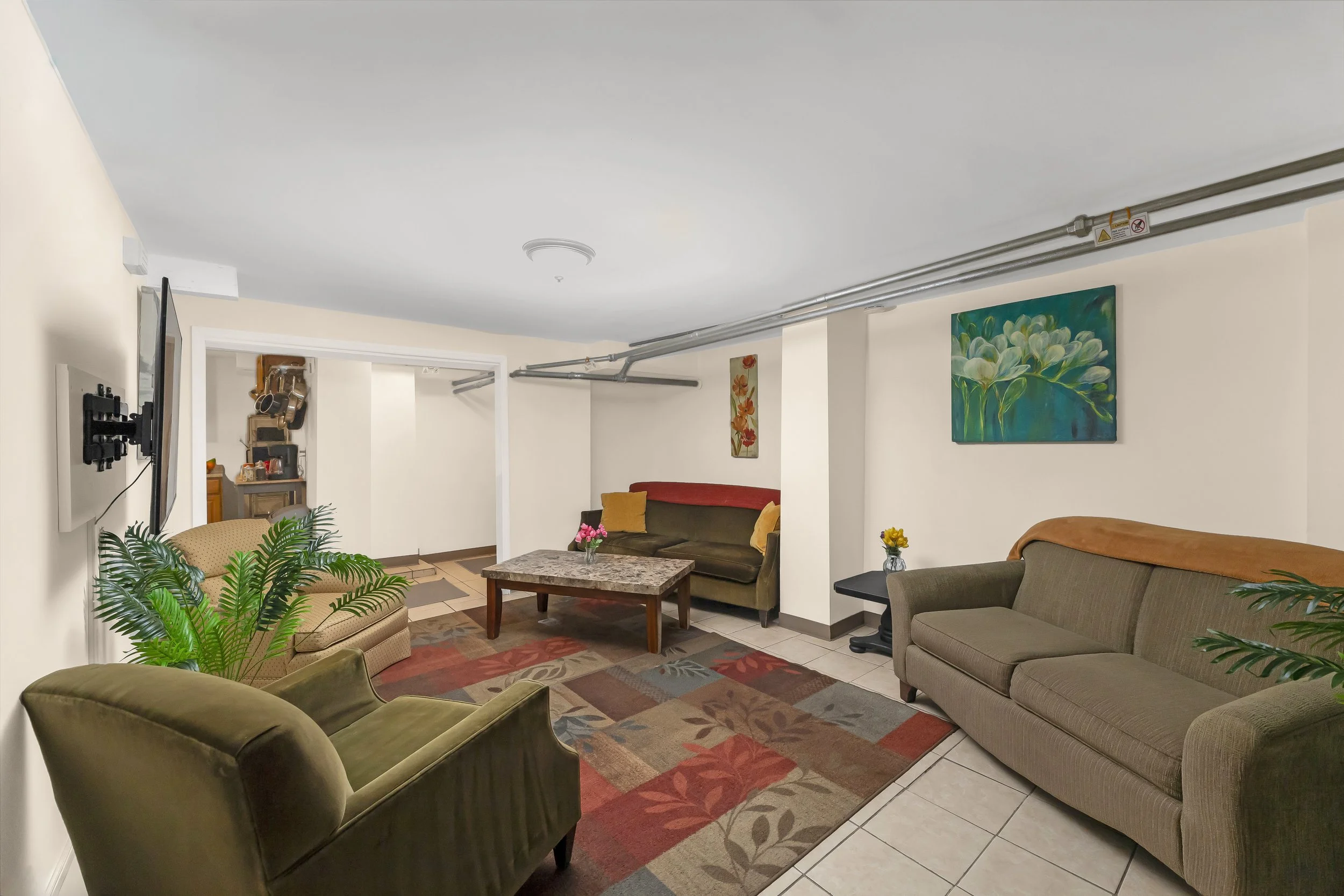 Living room with multiple sofas, a coffee table, colorful artwork, and potted plants.