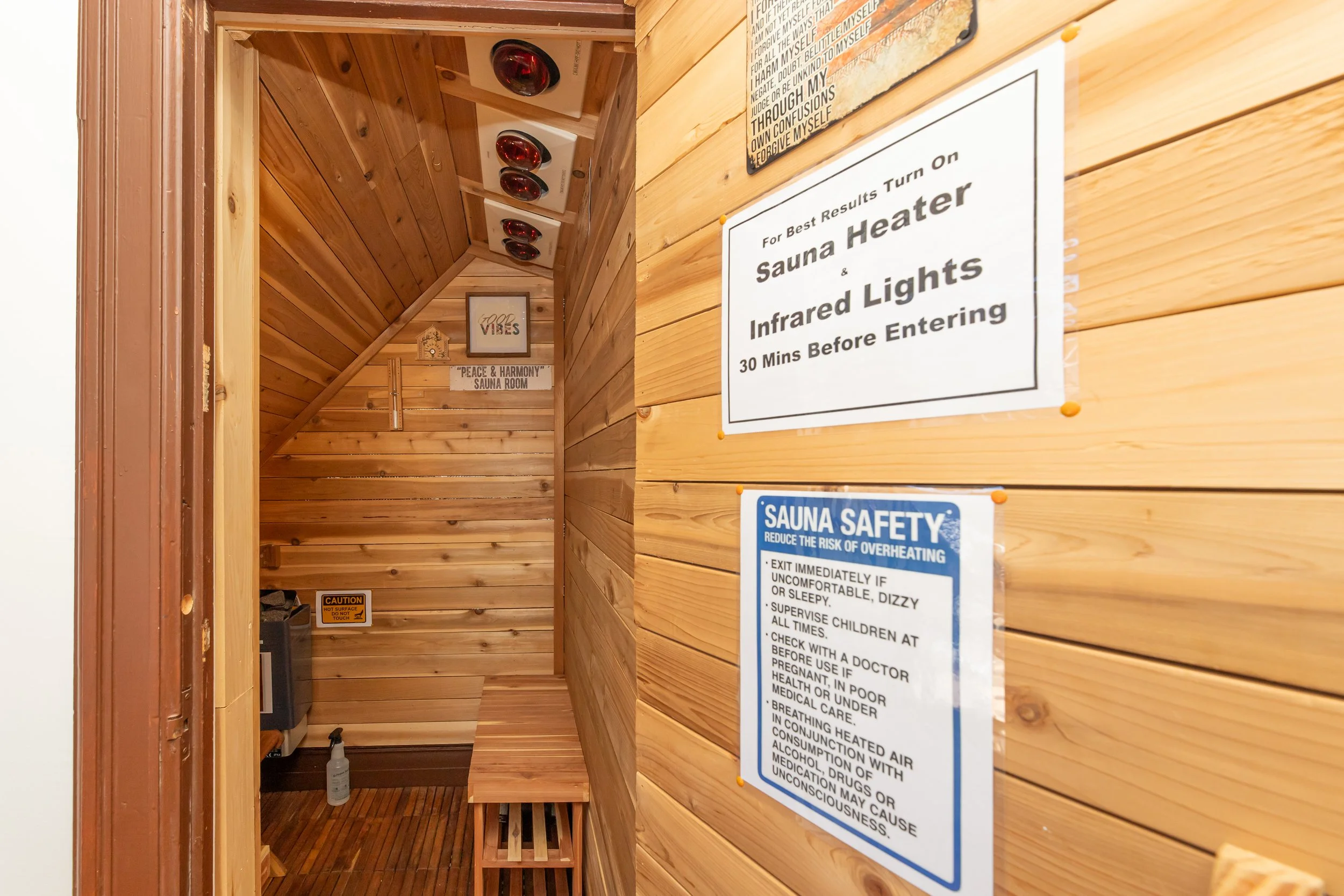 Wood-paneled hallway leading to sauna, with signs on wall including safety instructions and guidelines for using sauna heaters and infrared lights.
