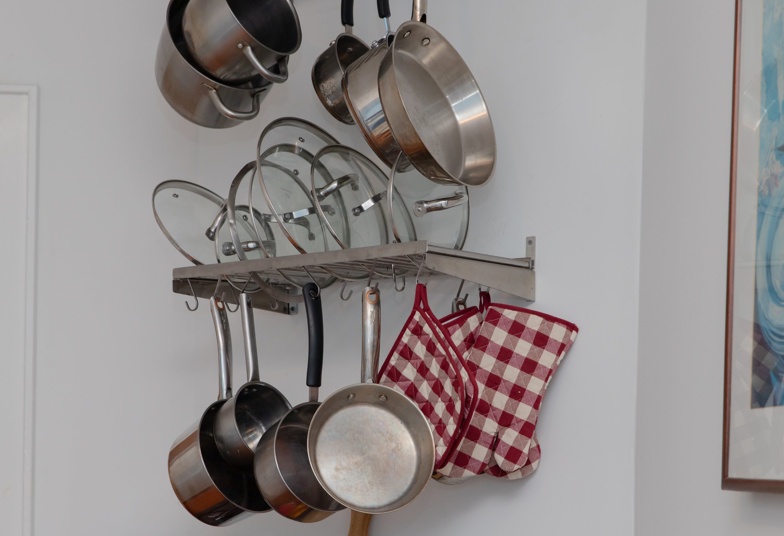 Metal pots and pans hanging on wall-mounted racks with red plaid oven mitts hanging on hooks.