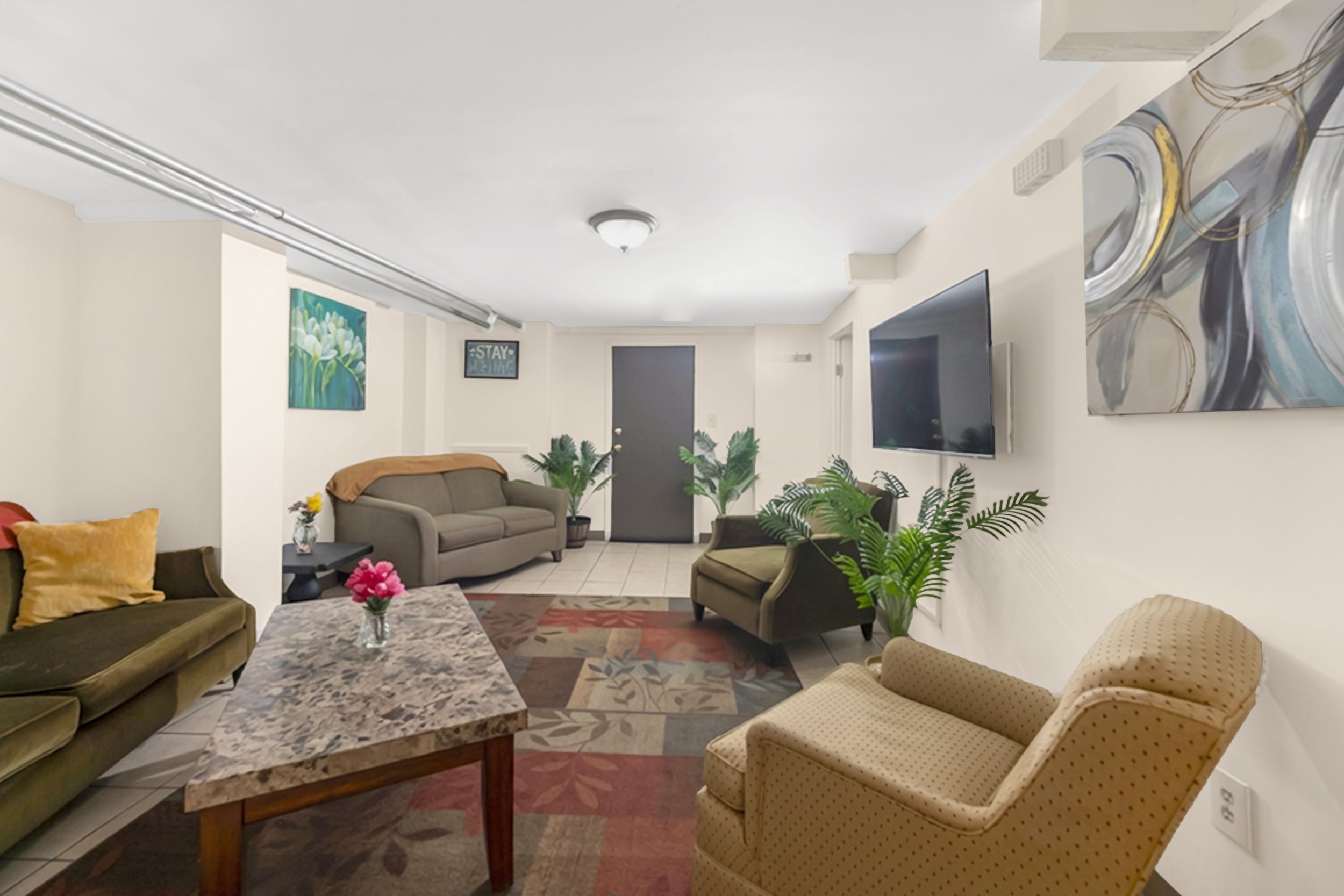 Living room with beige and green chairs, a marble coffee table, large TV on wall, and potted plants near front door.