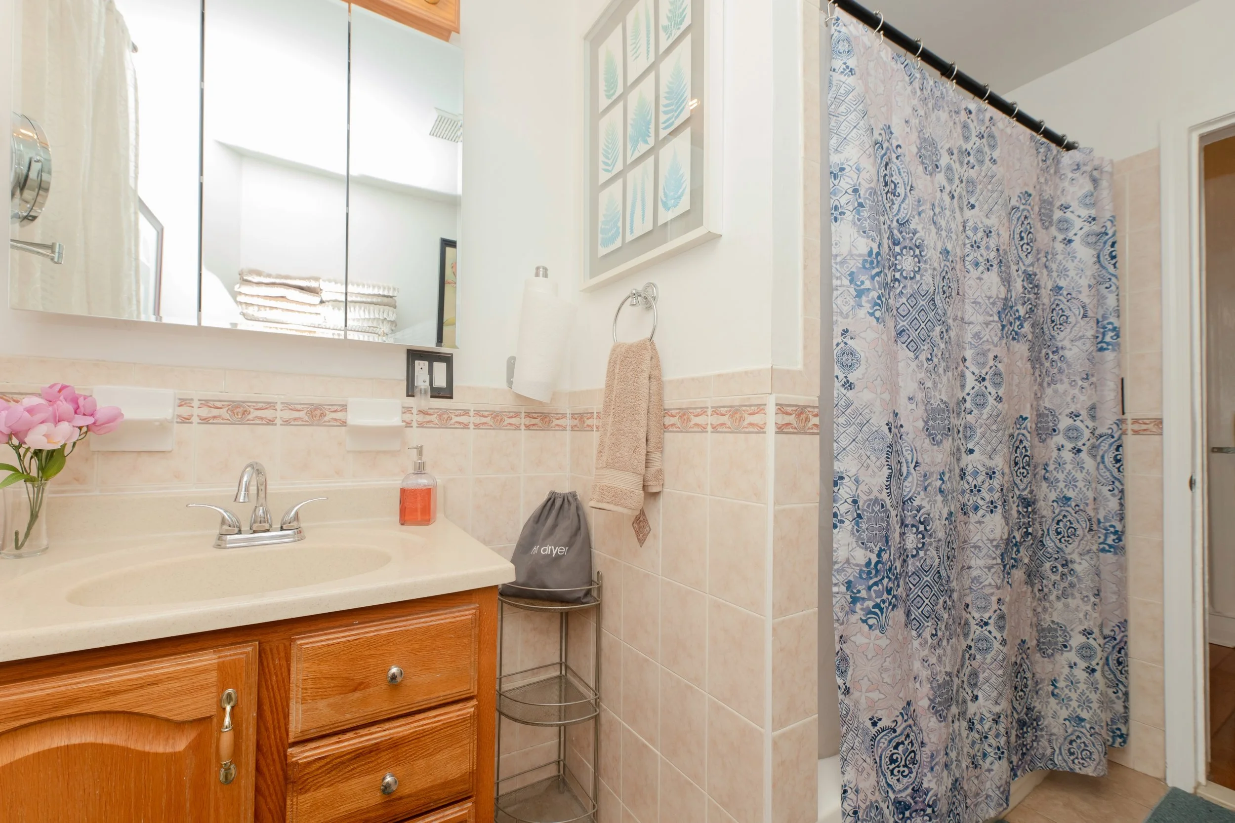 Bathroom with beige tile walls and a shower with a blue and white patterned curtain.