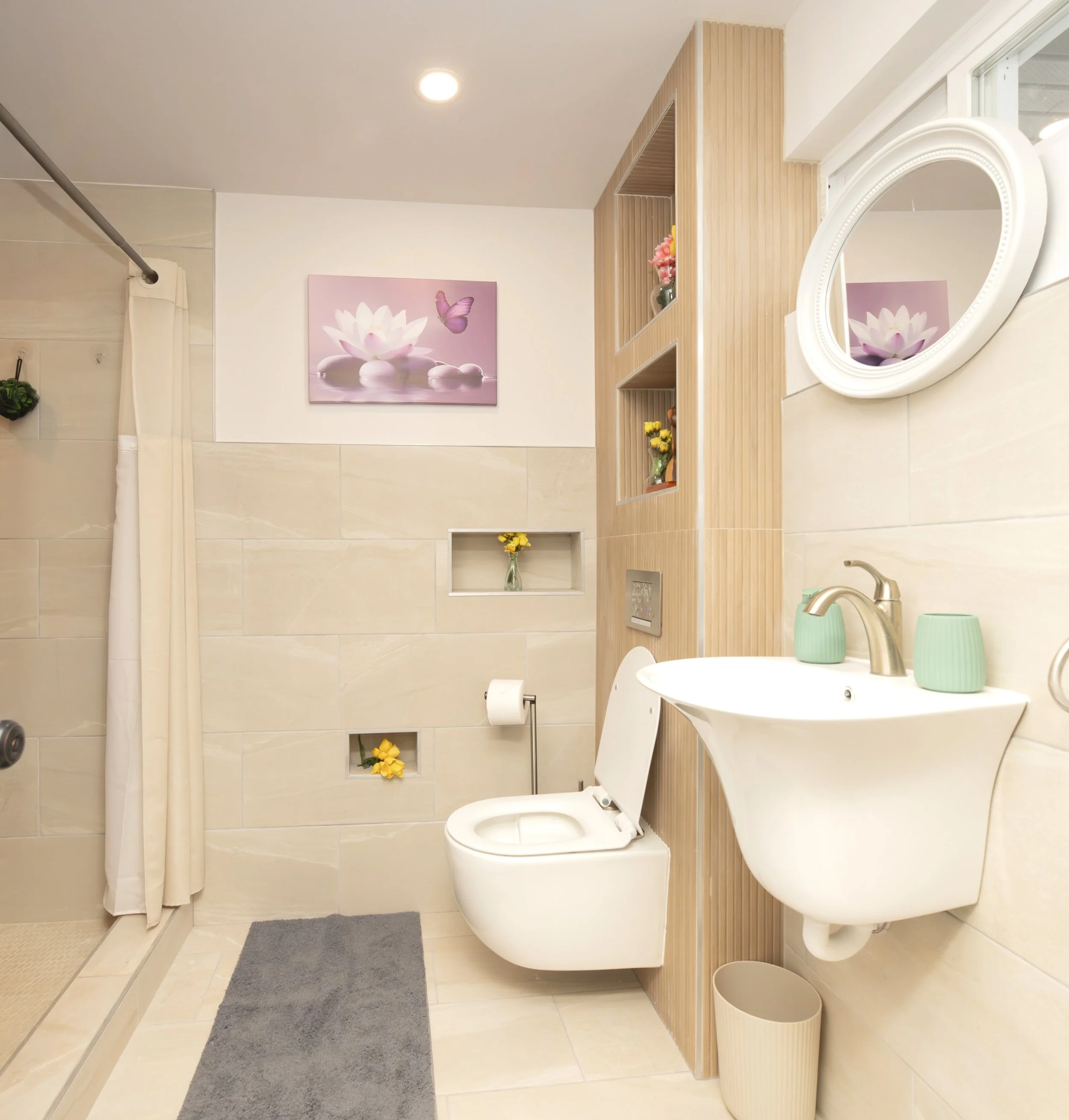 A bathroom featuring a shower area with a white curtain, a wall-mounted toilet, a small sink with a green cup and soap dispenser, decorative shelves with small vases and flowers, a framed lotus flower and butterfly art on the wall, and a small trash bin on the floor.