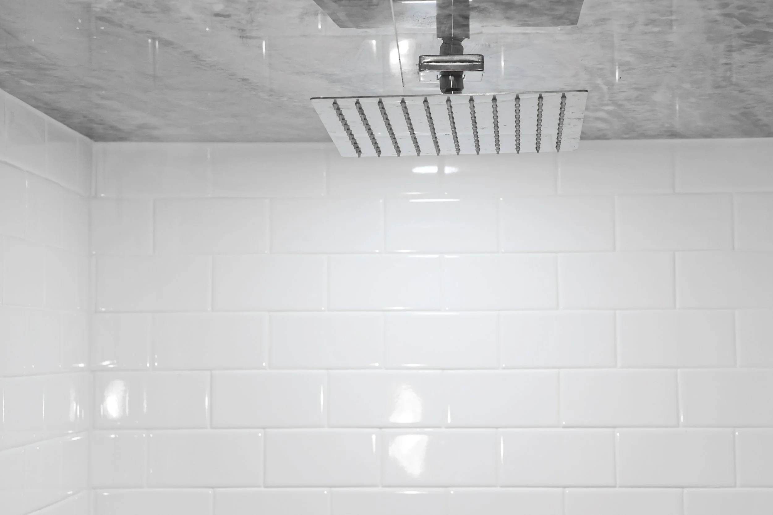 Close-up of a modern shower with white tiles on the walls, a ceiling-mounted rain shower head, and a shower arm in a bathroom.