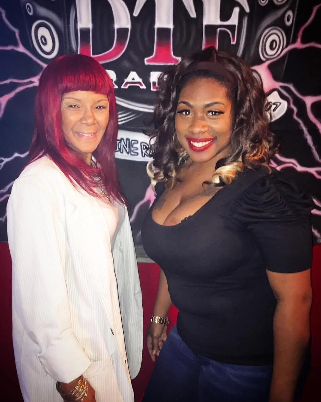 Two women smiling and posing for a photo in front of a black background with a logo and colorful design.