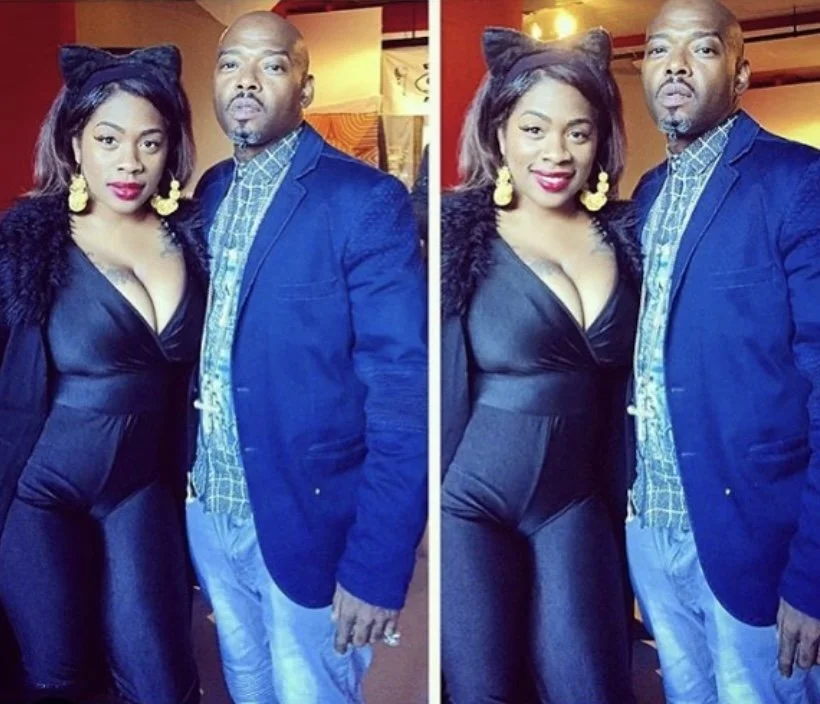 A woman and a man posing together, with the woman wearing black outfit, yellow earrings, and a headband with ears, and the man in a blue blazer with a checkered shirt, in a warmly lit indoor setting.