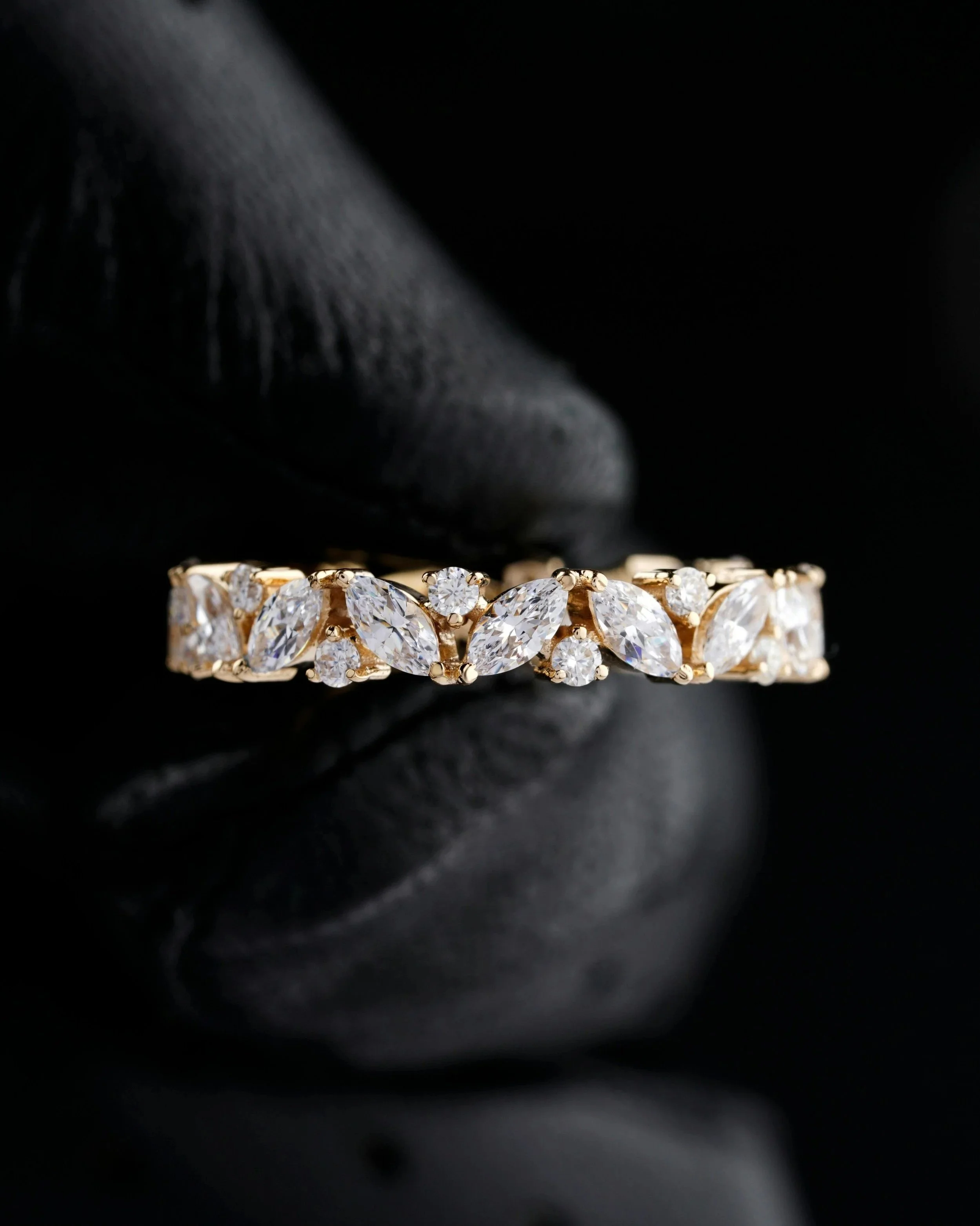 Close-up of a gold ring with multiple diamonds, held by a gloved hand against a dark background.