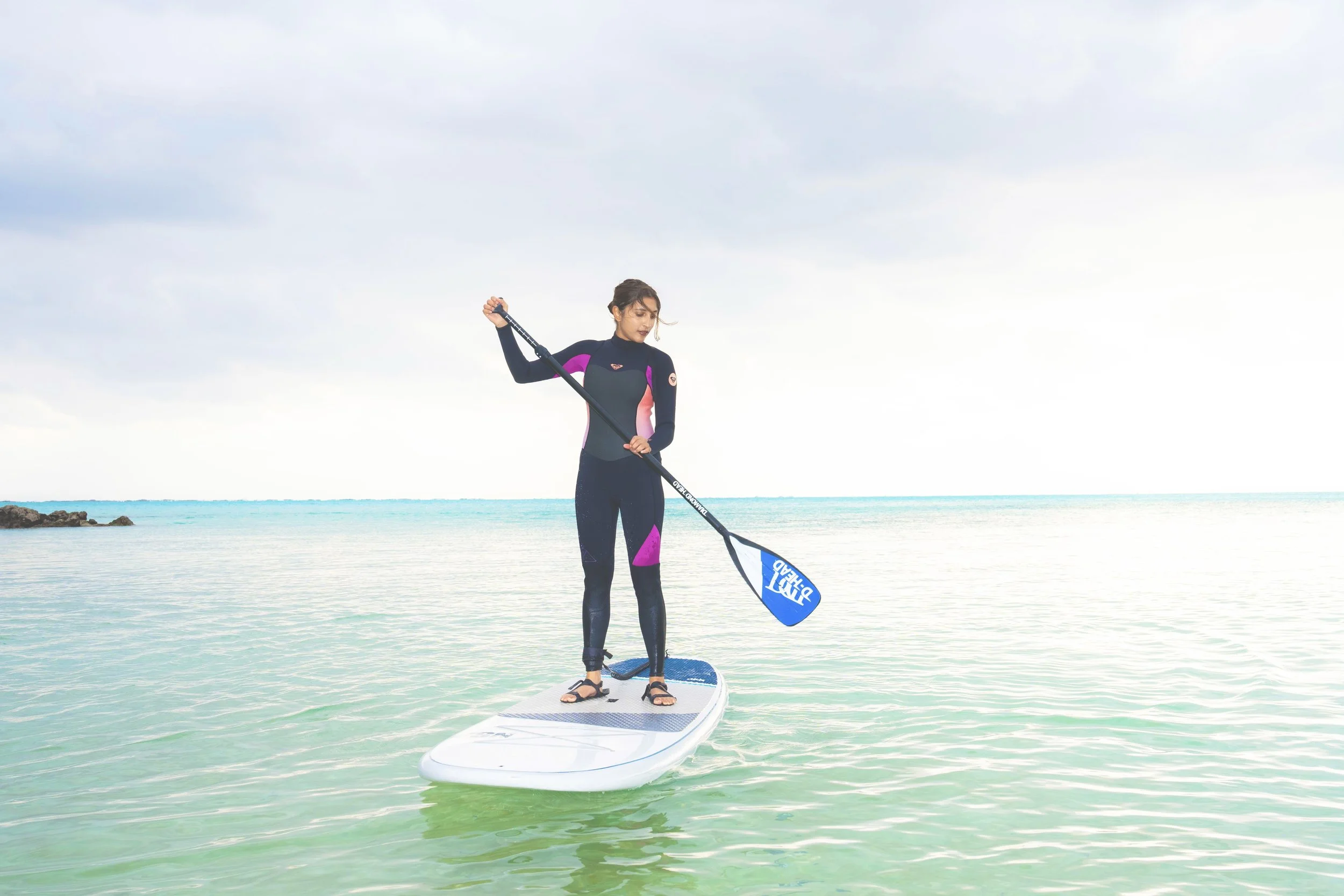Woman paddleboarding on calm water with sky and horizon in background.