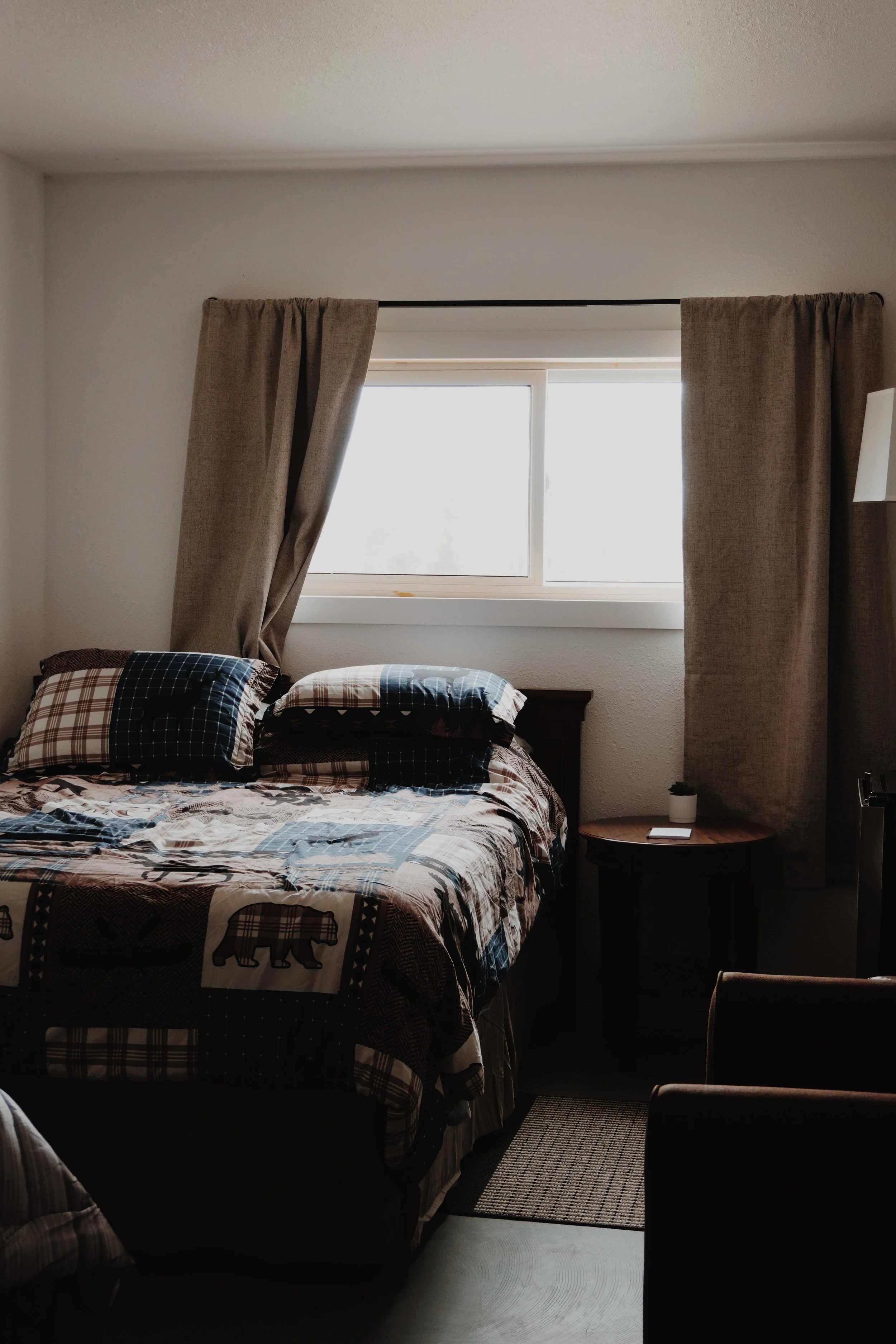 Part of a bed with a white pillow and crumpled sheets, and a wooden nightstand against a plain wall.