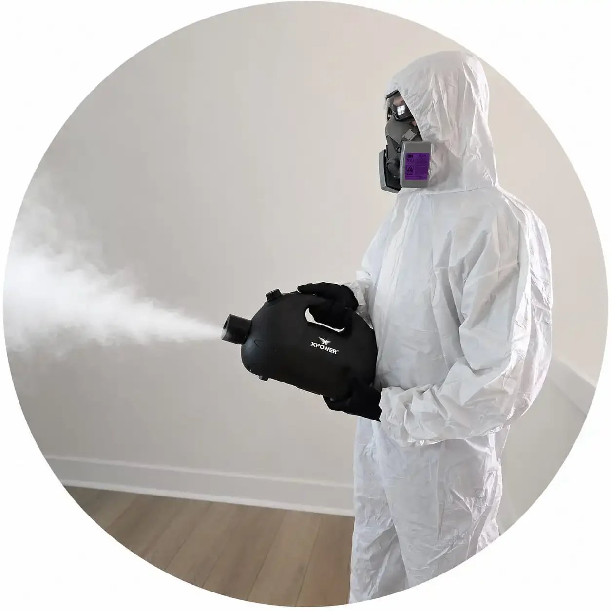 A man in dark clothing, glasses, and a cap is using a vacuum cleaner to clean a sofa in a living room.
