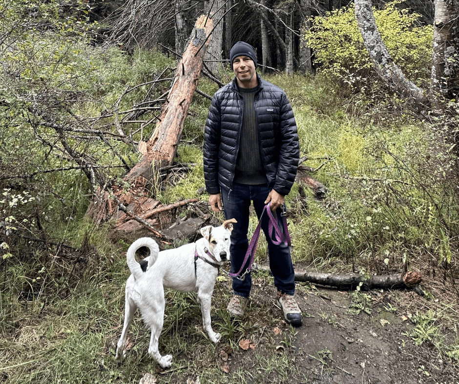man in beanie walking a white dog in the forest