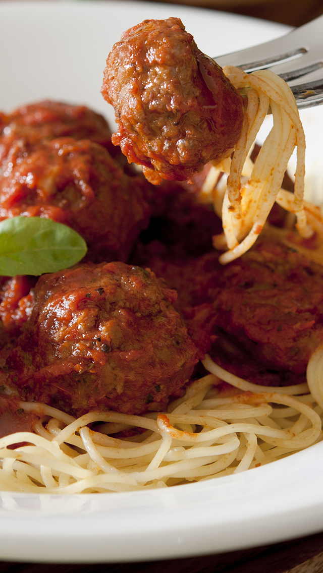 Spaghetti with meatballs on a white plate, topped with tomato sauce, with a fork lifting one meatball and spaghetti.