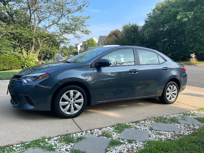 A dark gray sedan parked on a driveway with a residential neighborhood in the background.
