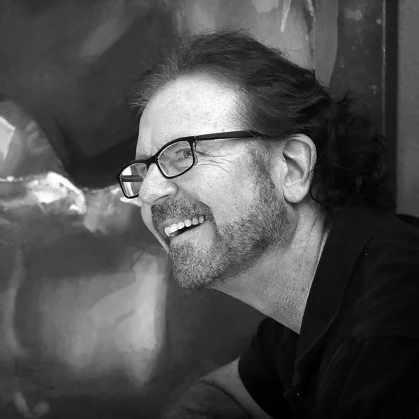 Artist Richard Hawk with glasses and a beard smiling and looking to the side in a black and white photo.