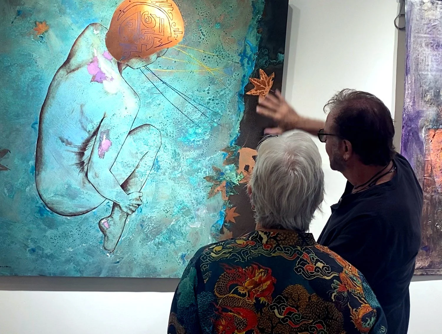 Artist explaining artwork on the wall of a gallery to a visitor