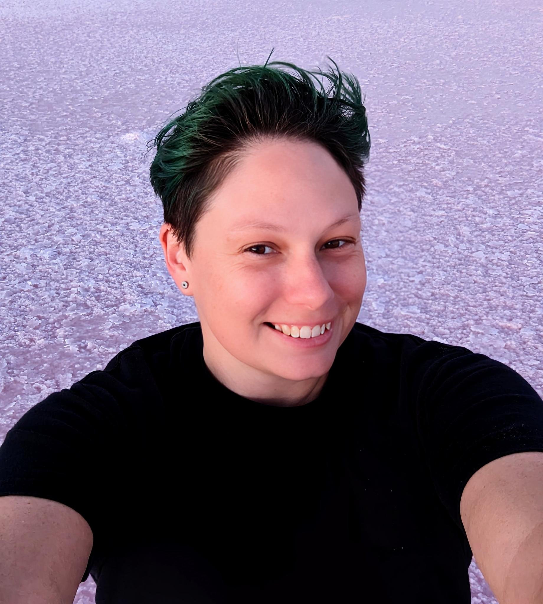 Person taking a selfie on Salt Flats with a pink hue, smiling, short dark hair, black shirt.