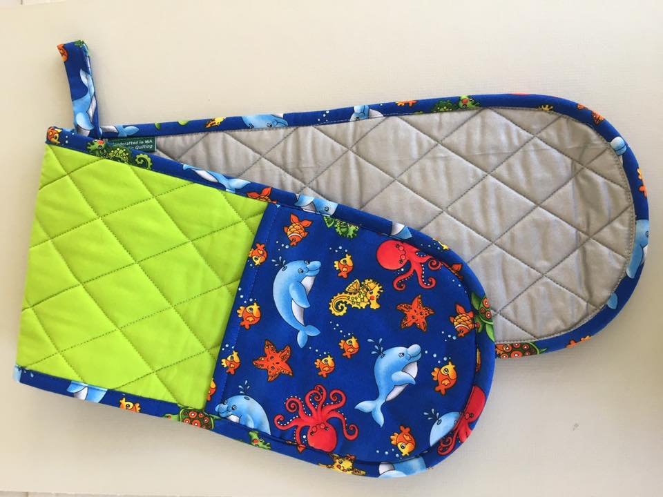 Colorful oven mitts with ocean creature patterns, featuring dolphins, starfish, octopuses, and fish, placed on a white surface.