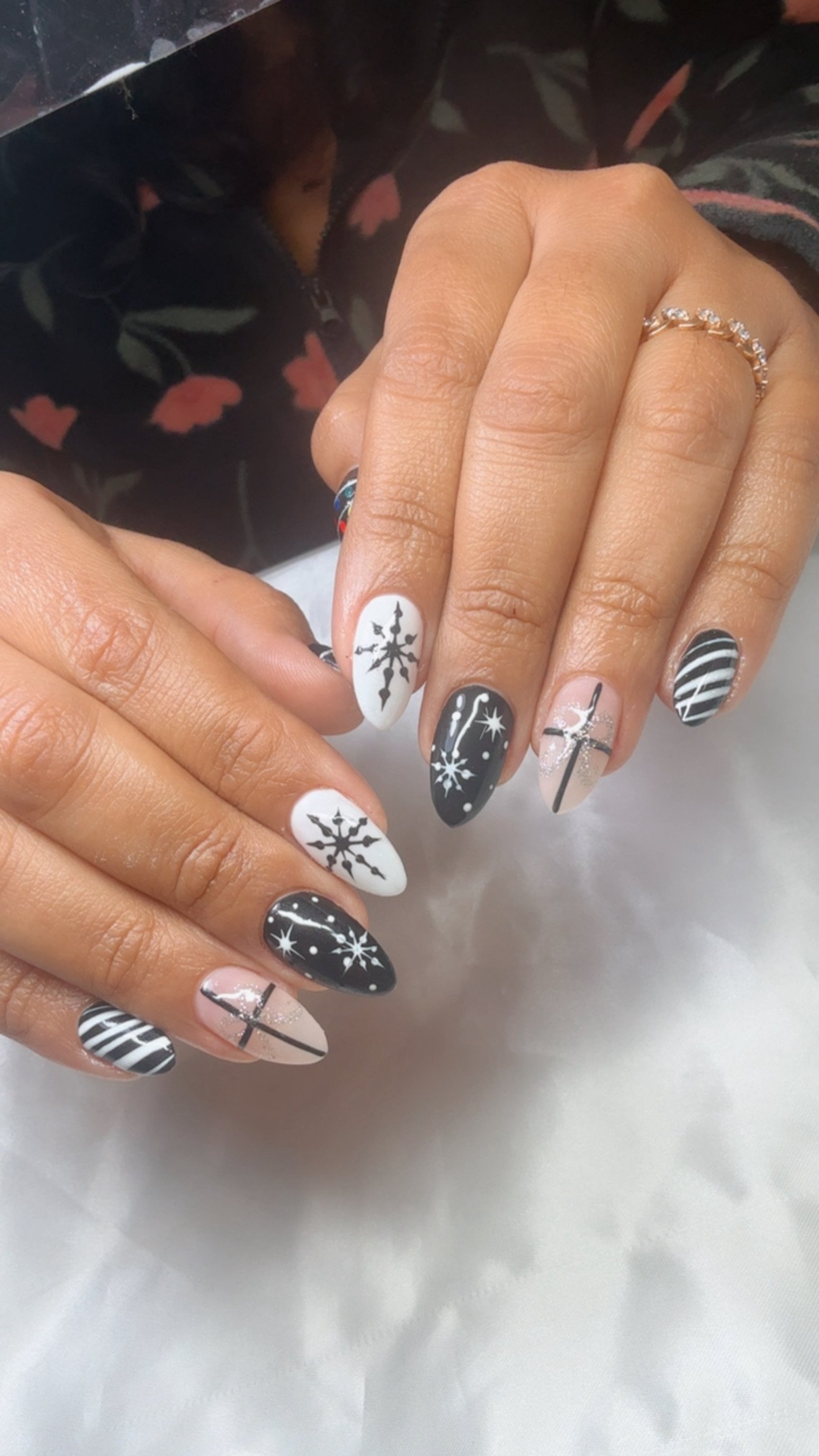 Close-up of hands with holiday-themed black and white nail art, including snowflakes, stars, and stripes, wearing rings.