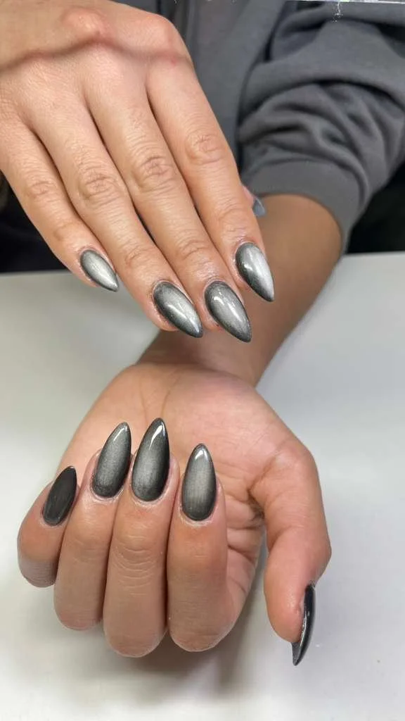 Close-up of two hands with metallic silver and charcoal black gradient acrylic nails, resting on a white surface.