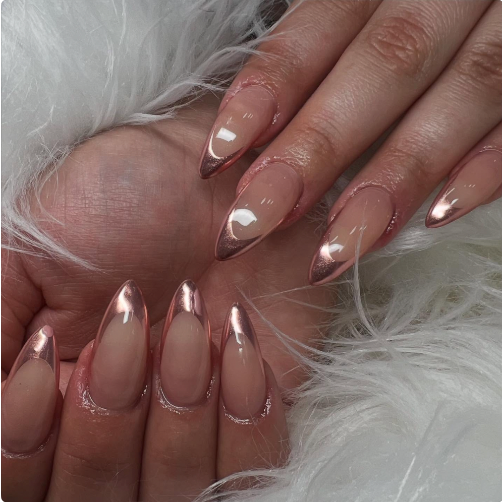 Close-up of hands with well-manicured nails featuring a nude base and metallic rose gold tips, surrounded by white fluffy fabric.