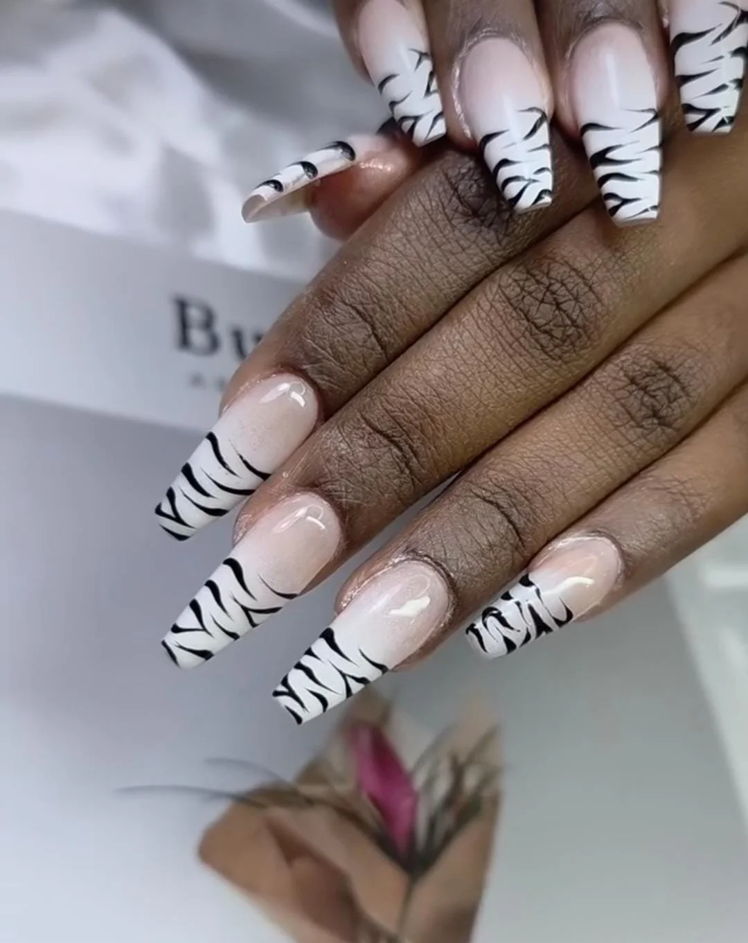 Close-up of a hand with long square-shaped nails featuring zebra-striped black and white nail art.