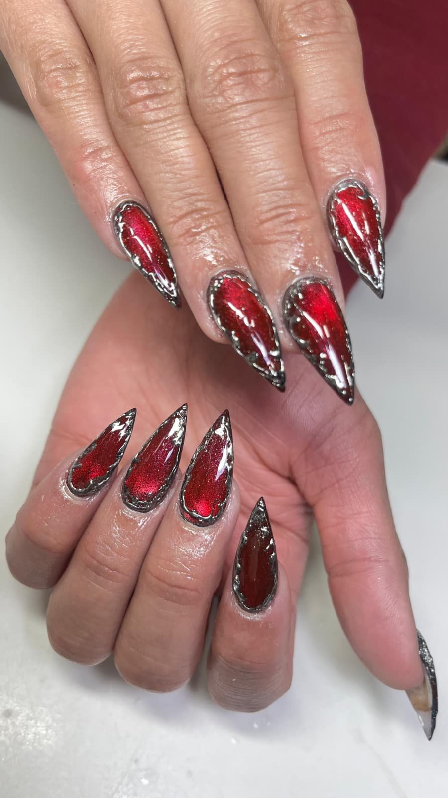 Close-up of hands with decorated long, pointed, red and black metallic nails.