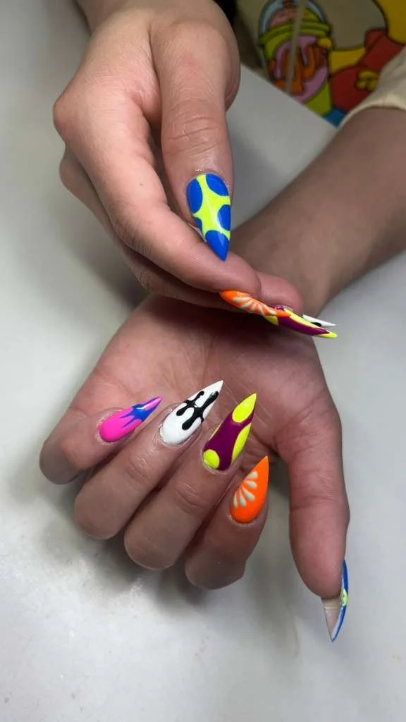 Close-up of hands with colorful, decorative nails featuring various bright patterns and colors.