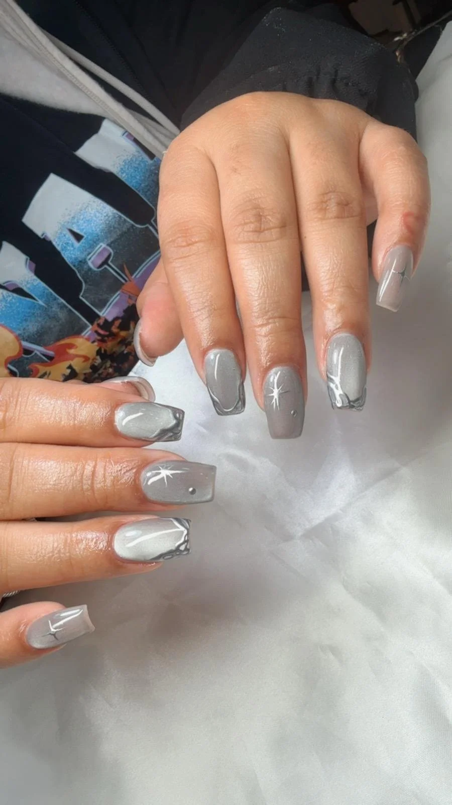 Woman with silver and gray marbled manicure with white starburst designs on some nails.
