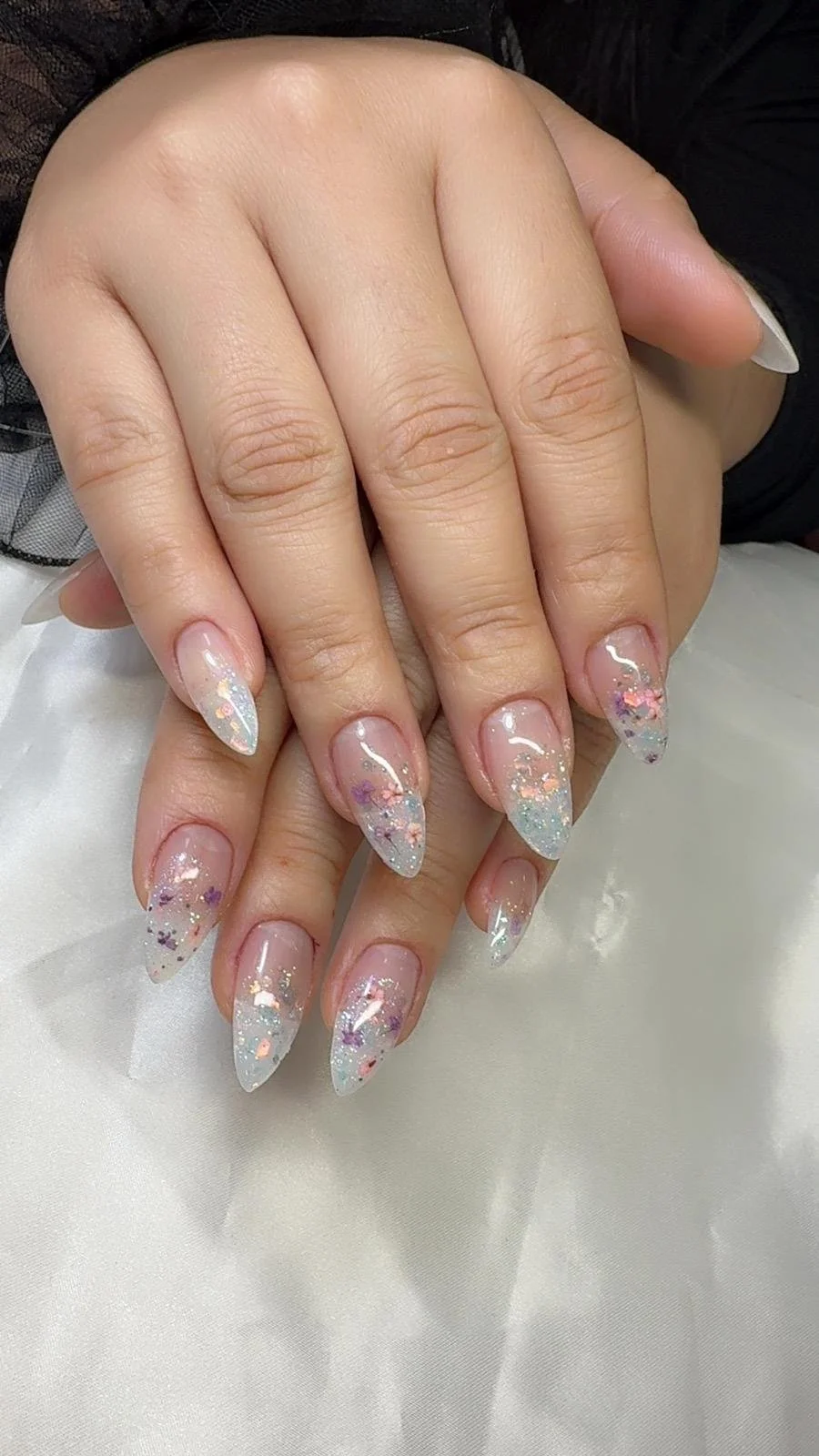 Close-up of hands with decorated acrylic nails featuring glitter and colorful floral designs.