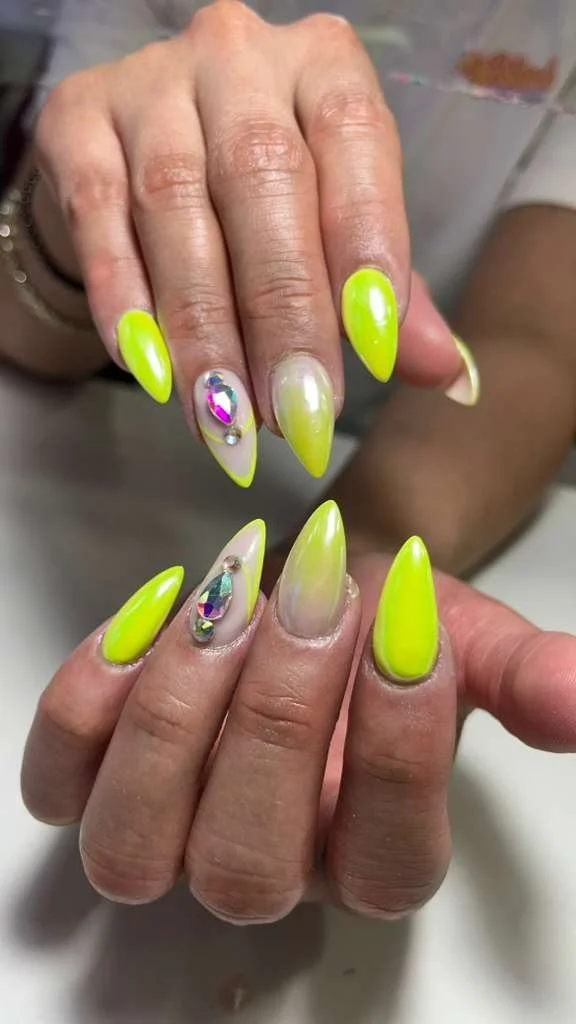 Close-up of two hands showcasing neon yellow and clear acrylic nails with rhinestone and bead decorations.
