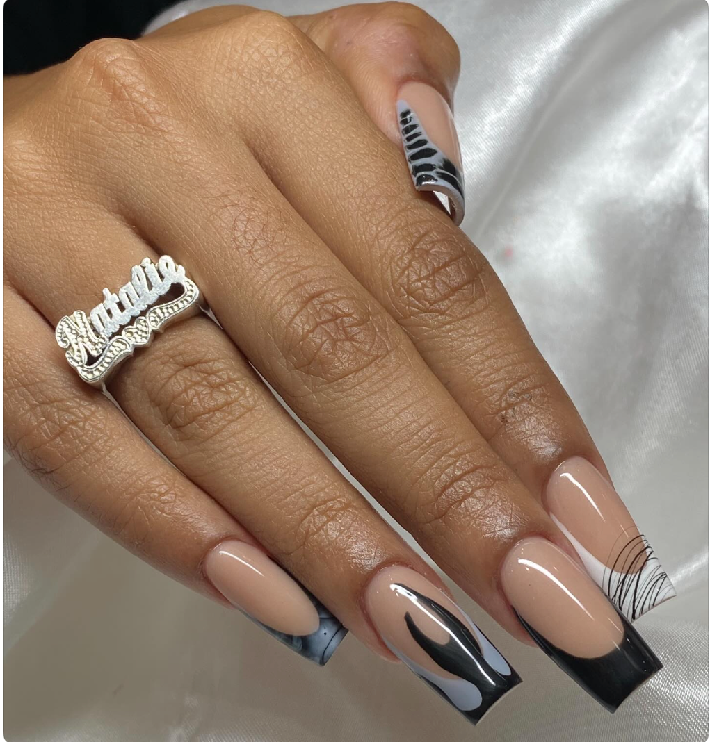 Close-up of a hand with manicured nails painted in nude, black, and marble design, wearing a silver ring that says "Miami."